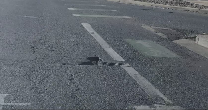 A frame of cracked asphalt with a pothole opening across a lane line