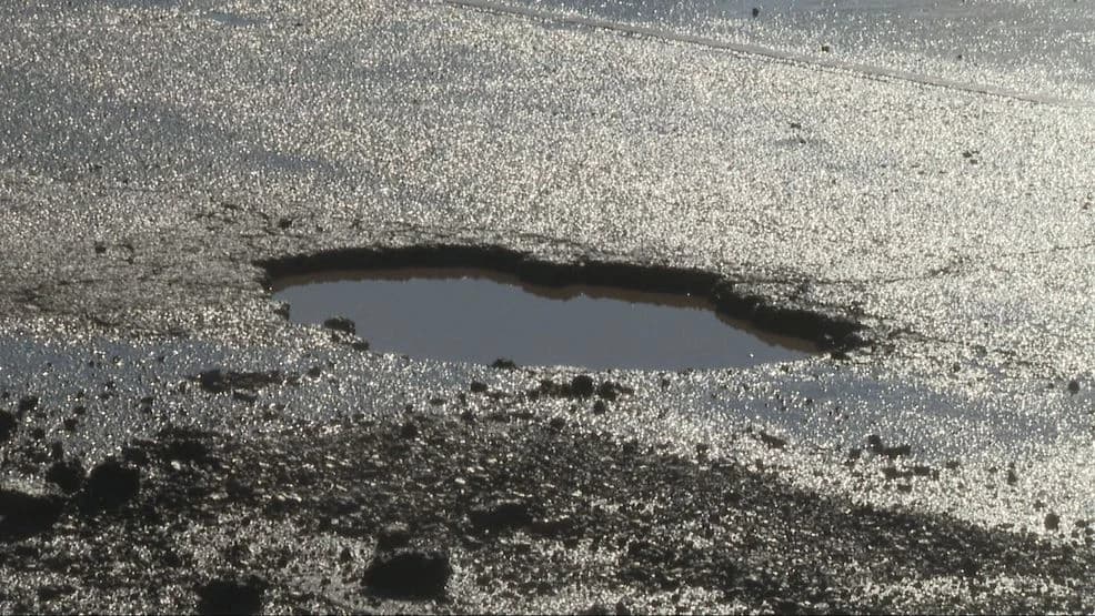 Water-filled pothole in a backlit asphalt road surface